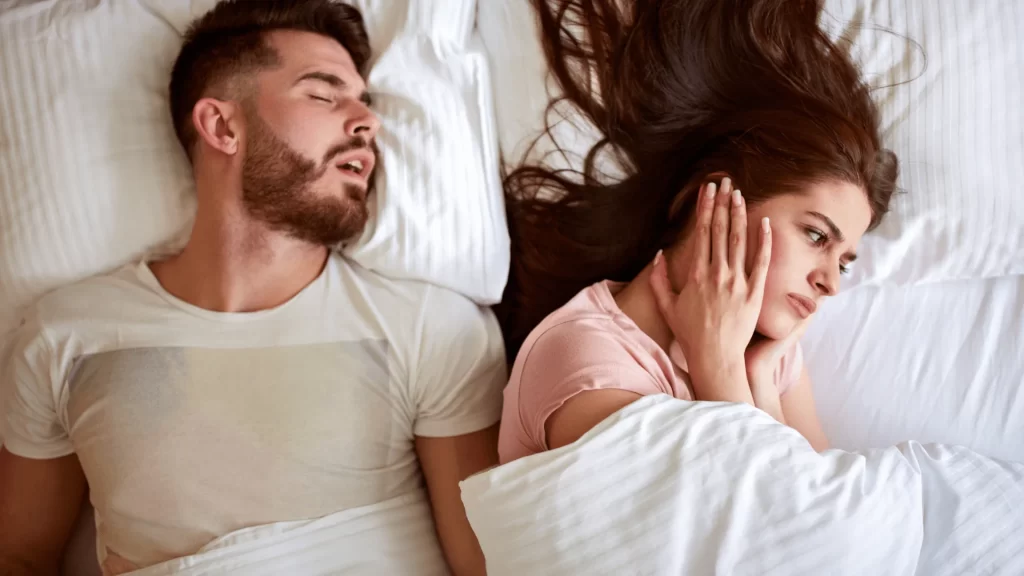Lovos partnerė prisidengia ausis šalia miegančio vyro
